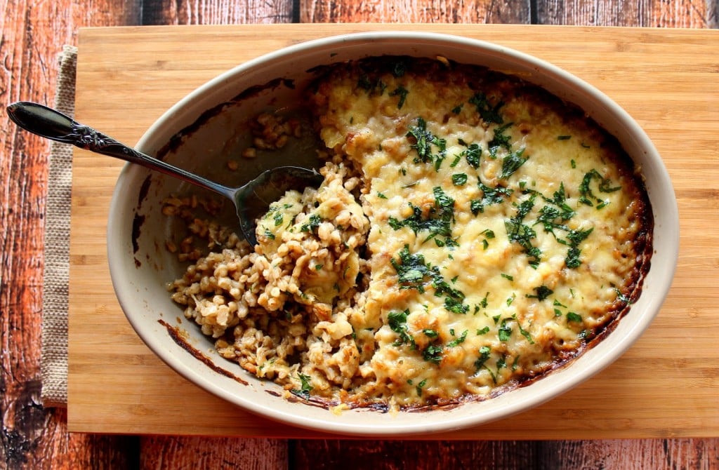 A serving spoonful of Cheesy Farro and Onion Bake being lifted from a casserole dish.