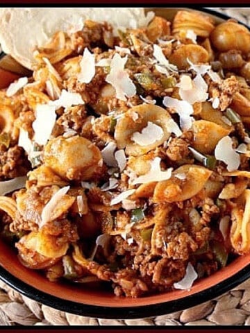 Orecchiette with Meat Sauce in a bowl with a spoon and Parmesan cheese.