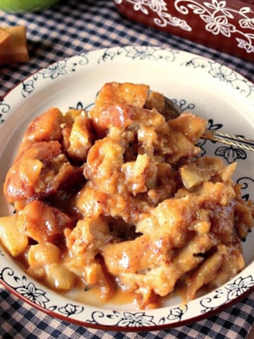 A plate filled with Caramel Apple Bread Pudding with a few caramels in the background.