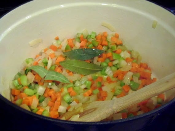 Diced carrots, celery and onion in a pot with bay leaves and a wooden spoon.
