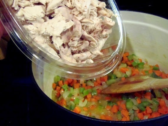 Diced chicken being added to a soup pot with vegetables.