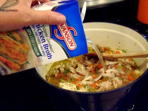 Chicken broth being added to a pot of Carrot Ginger Chicken Noodle Stew.