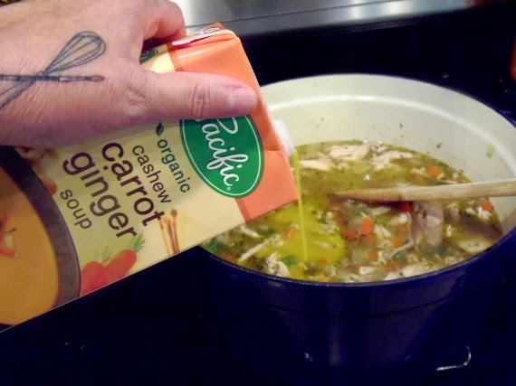 A carton of carrot ginger soup being added to a soup pot.