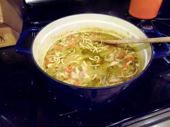 A soup pot with egg noodles and Carrot Ginger Chicken Noodle Stew.