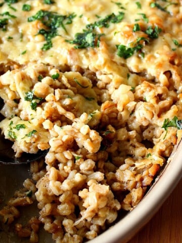 An overhead photo of a cheese topped Farro and Onion Casserole with a serving spoon and chopped parsley.