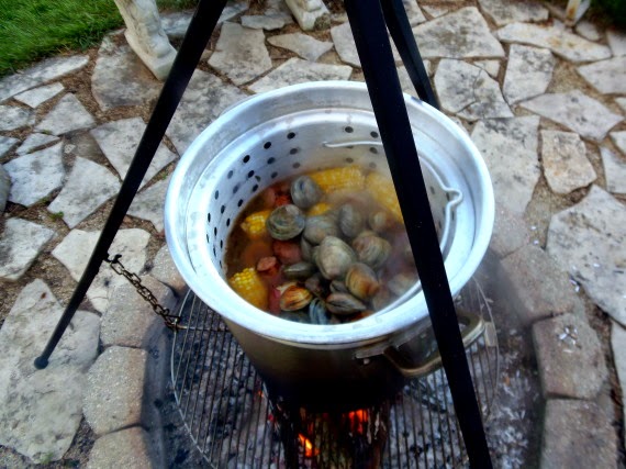 Looking inside of a huge pot of seafood and corn cooking over an outdoor firepit.