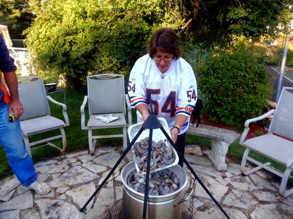 Person adding shrimp into a huge pot cooking over an outdoor firepit.