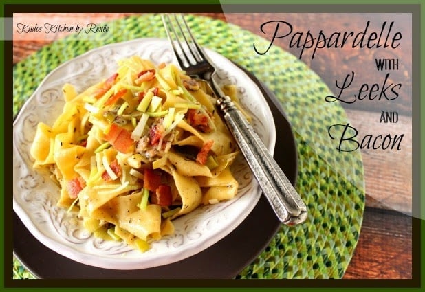 A horizontal framed title text photo of pappardelle pasta recipe with leeks and bacon in a while bowl on a green place mat with a fork.