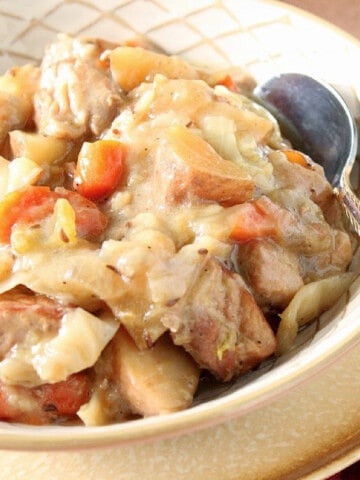 A creamy serving of Pork and Cabbage Stew in a bowl with a spoon.