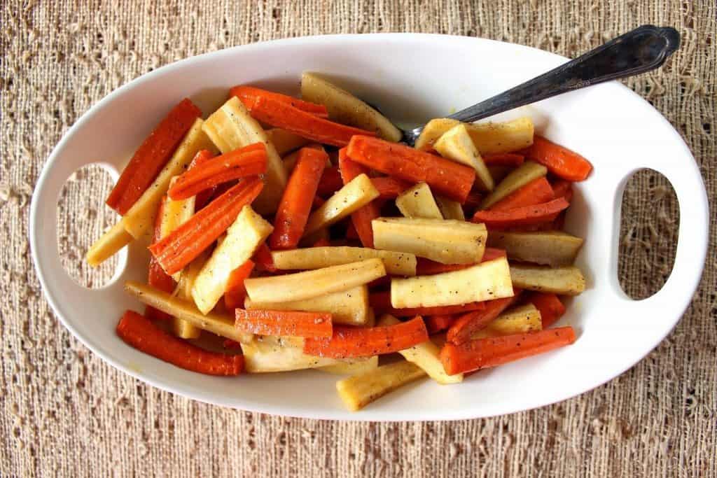 Overhead horizontal photo of an oval white dish with roasted carrots and parsnips and a serving spoon.