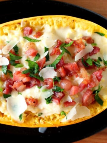 On overhead photo of a cut in half Spaghetti Squash Alfredo with tomatoes and fresh basil.