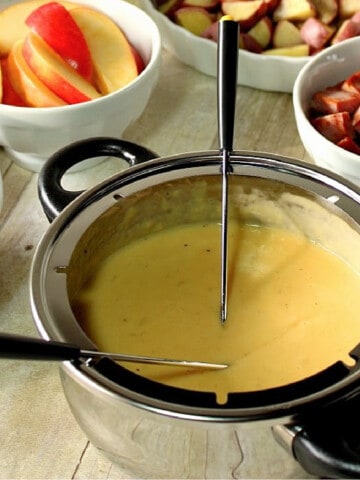 A silver fondue pot filled with Swiss Cheese Fondue and two fondue forks.