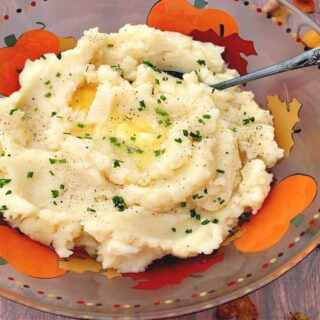 An overhead photo of a colorful bowl filled with Celery Root Mashed Potatoes along with a spoon and autumn leaves.