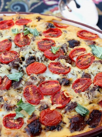 A colorful Lasagna Strata in a casserole dish with fresh basil, tomatoes, and sausage.