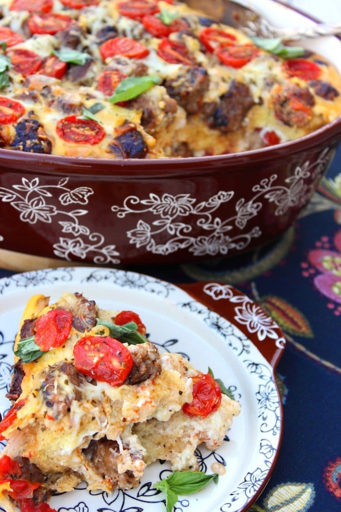 A colorful serving Lasagna Strata in a casserole dish with fresh basil, tomatoes, and sausage.