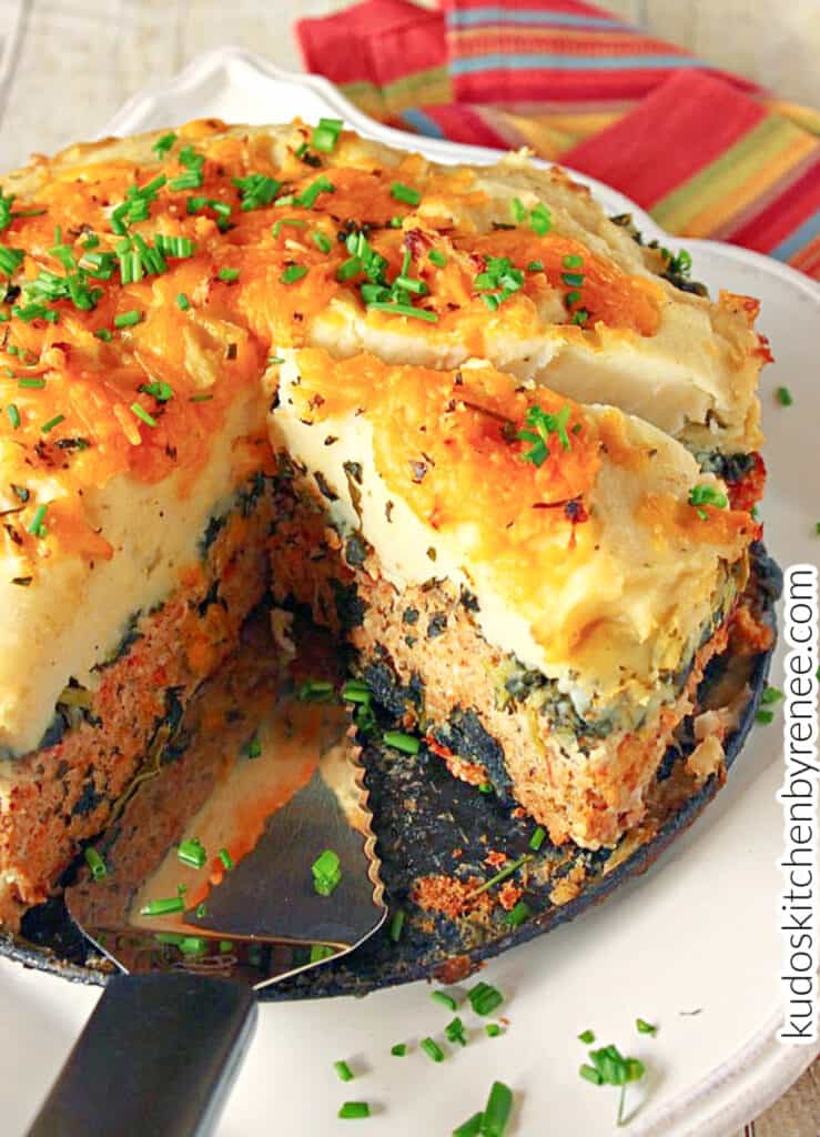 A vertical closeup of the inside of a Layered Turkey Meatloaf with kale, mashed potatoes, cheese, and chives.