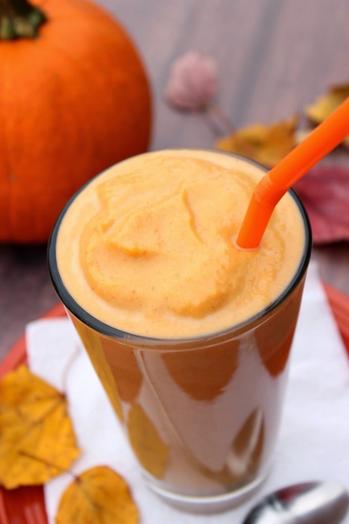 A tall glass filled with a Low Calorie Pumpkin Pie Milkshake and an orange straw.