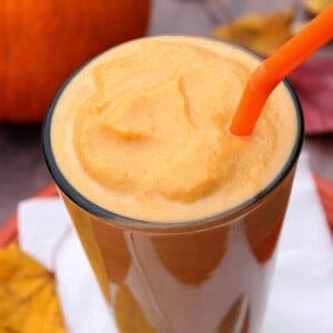 A tall glass filled with a Low Calorie Pumpkin Pie Milkshake and an orange straw.