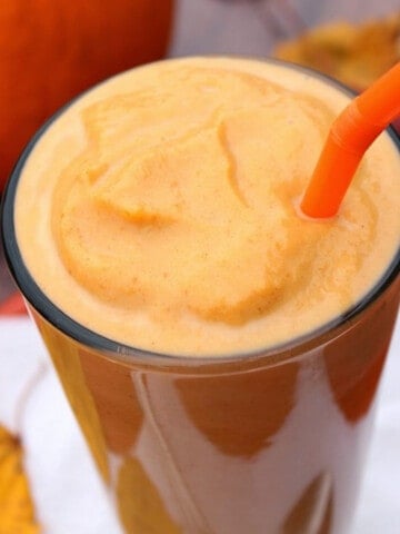 A tall glass filled with a Low Calorie Pumpkin Pie Milkshake and an orange straw.