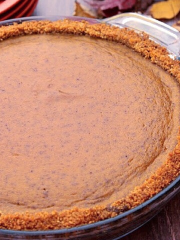 A Pumpkin Praline Pie with autumn leaves in the background.