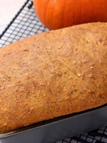 A loaf of Pumpkin Spice Yeast Bread in a loaf tin on a cooling rack.