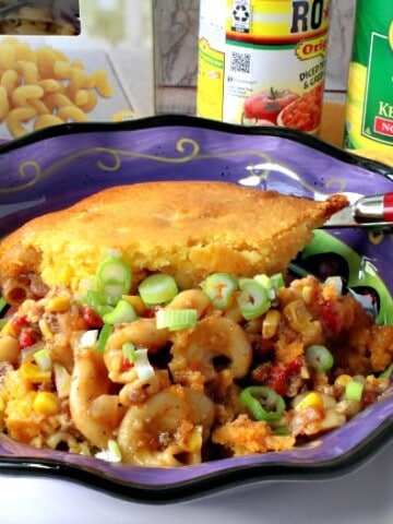 A purple bowl filled with chili mac with a cornbread crust along with a spoon.