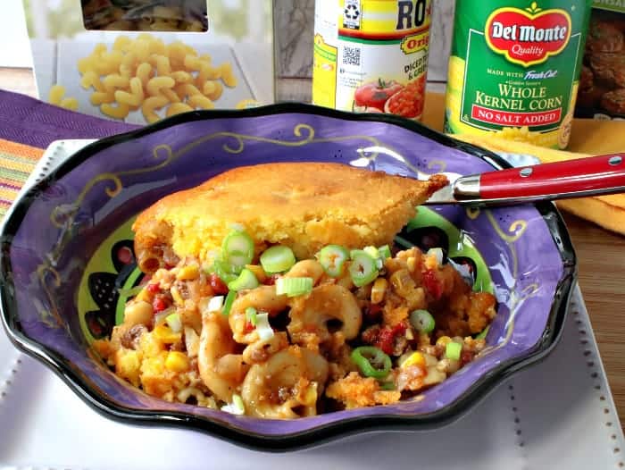 A purple bowl filled with chili mac with a cornbread crust along with a spoon.
