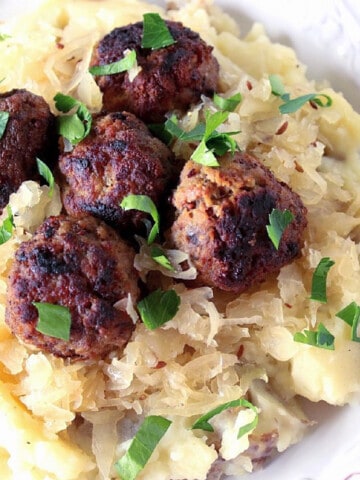 A serving of German Meatballs with Potatoes and Sauerkraut topped with fresh parsley.