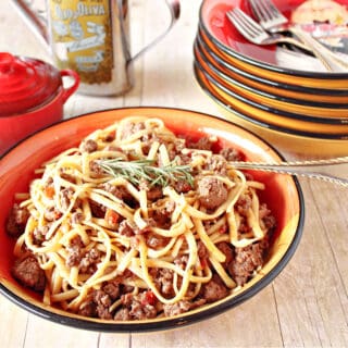 A bowl filled with Linguine with Lamb along with a fork and a stack of bowls in the background.