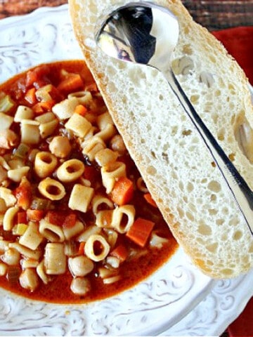 An offset horizontal photo of a bowl of Tuscan Pasta Soup with a slice of bread and a spoon on the side.