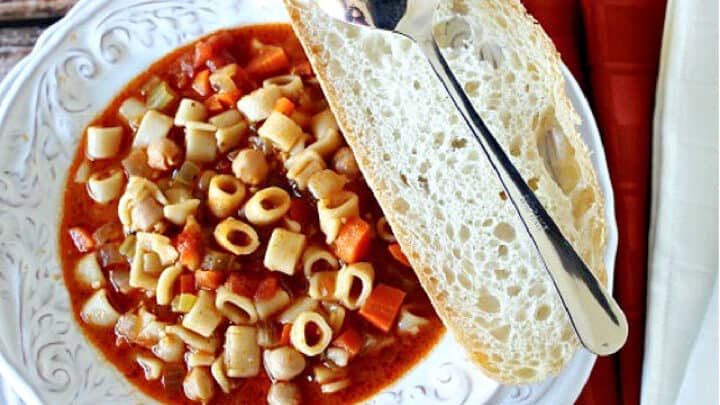 An offset horizontal photo of a bowl of Tuscan Pasta Soup with a slice of bread and a spoon on the side.