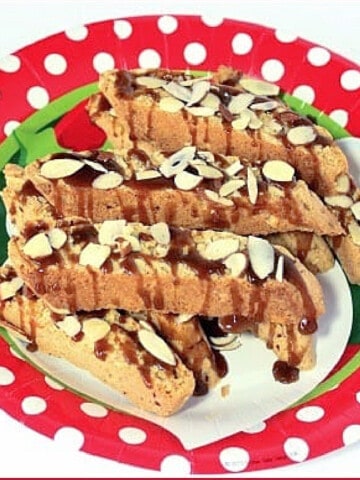 A stack of Amaretto Coconut Biscotti on a red and white polka dot plate and the cookies are drizzled with caramel.