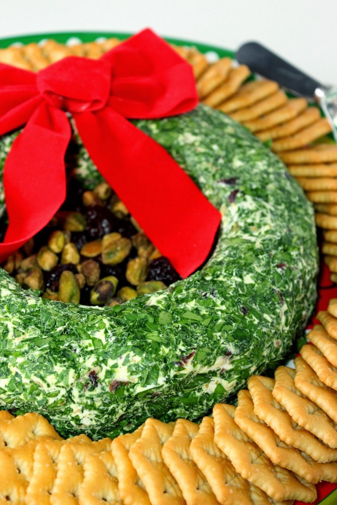 Closeup vertical photo of a Christmas wreath appetizer made out of goat cheese, with pistachios, dried cherries and parsley.