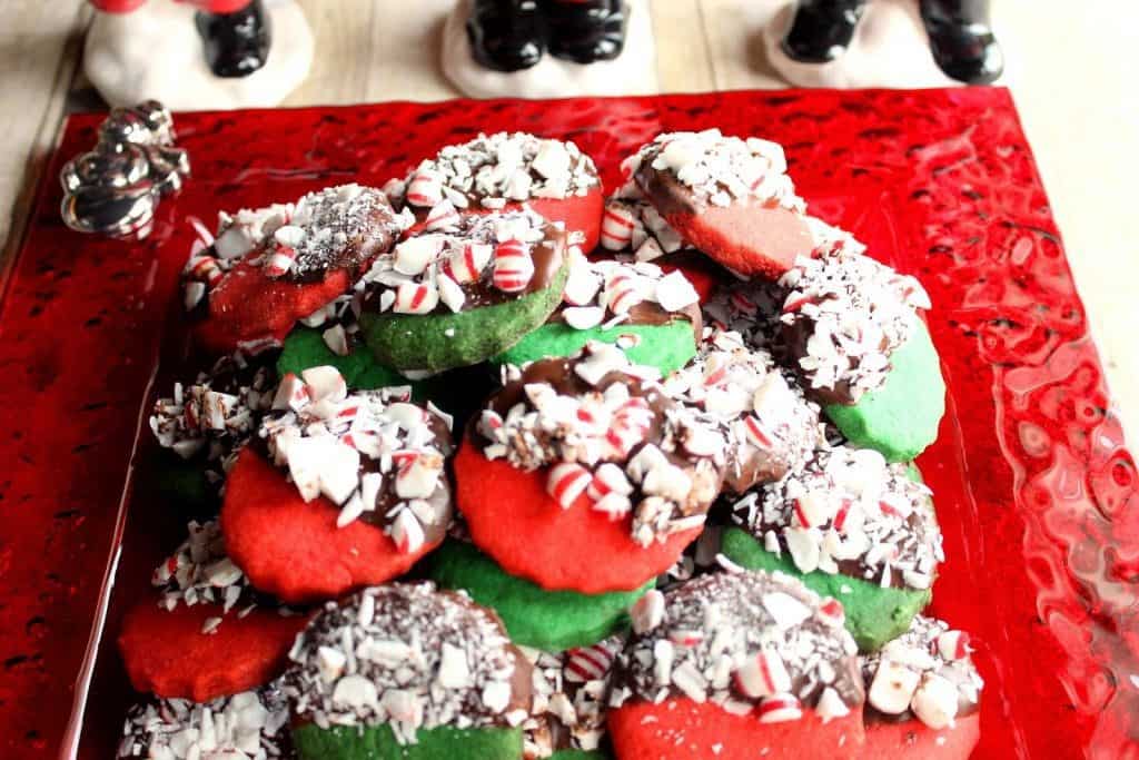 A bunch of red and green Peppermint Shortbread Cookies dipped in chocolate and peppermint on a red plate.