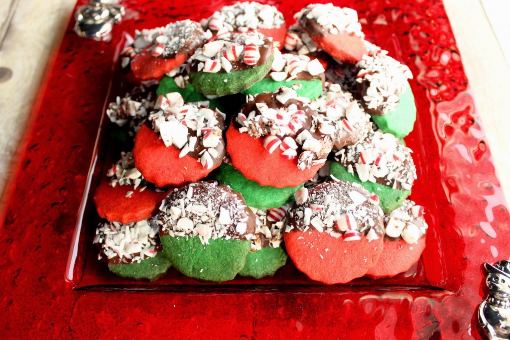 A bunch of red and green Peppermint Shortbread Cookies dipped in chocolate and peppermint on a red plate.