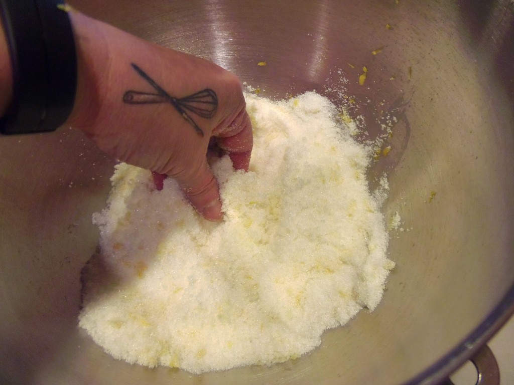 A hand in a bowl of sugar and lemon zest.