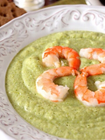 A white bowl filled with green Roasted Vegetable Soup with shrimp on top.