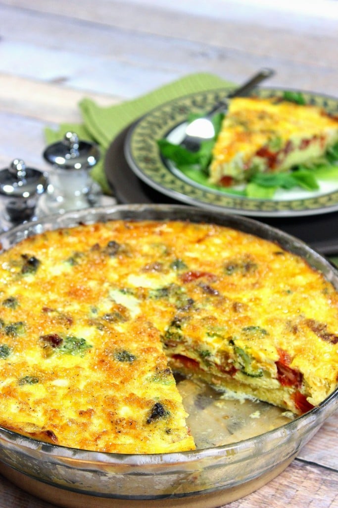 A vertical image of a spaghetti squash quiche in a pie plate with a slice taken out and a salt and pepper shaker in the background.