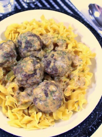 A plate of Low Fat Swedish Meatballs over egg noodles along with a spoon.