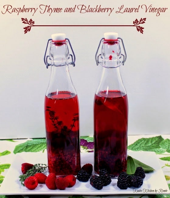 Two tall bottles filled with Homemade Berry Infused Vinegar on a white plate with fresh berries and herbs.