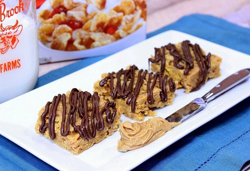 A white rectangle plate with three tiger paws cereal bars including a chocolate drizzle and a knife with peanut butter on it.