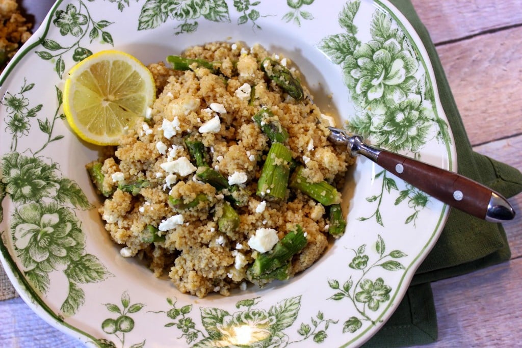 A pretty green and white bowl filled with Couscous Salad with Feta and Asparagus and a serving spoon.