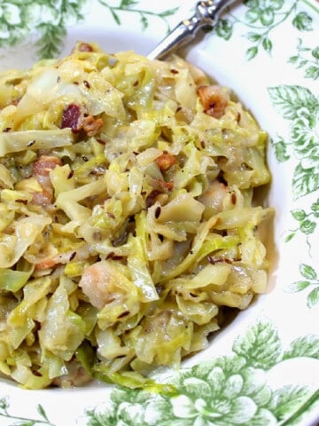 A green and white bowl filled with Creamed Cabbage with Bacon and Caraway and a spoon.