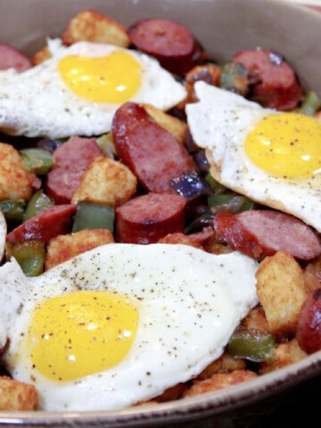 A casserole dish filled with Tater Tot Casserole, sausage and fried eggs.