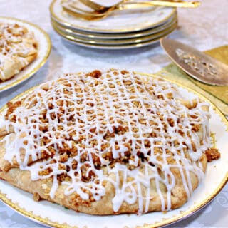 An Apple Crumble Crostata in the foreground with a stack of china plates and some gold napkins in the background.