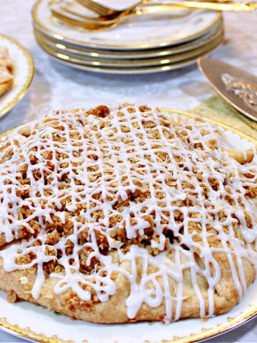 An Apple Crumble Crostata in the foreground with a stack of china plates and some gold napkins in the background.