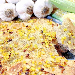 A Garlic Focaccia with Sweet Corn on a sheet tray along with garlic bulbs and fresh corn in the background.