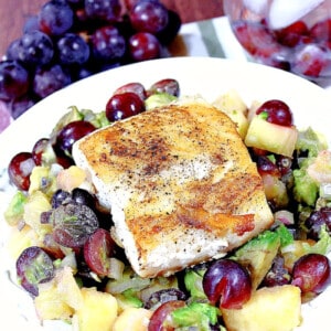 A dish of Mahi Mahi with grape and avocado salsa on a white plate with a bunch of grapes in the background.