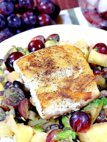 A dish of Mahi Mahi with grape and avocado salsa on a white plate with a bunch of grapes in the background.