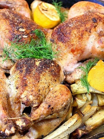 Three Roasted Cornish Hens with Fennel in a skillet with lemons and fennel fronds.